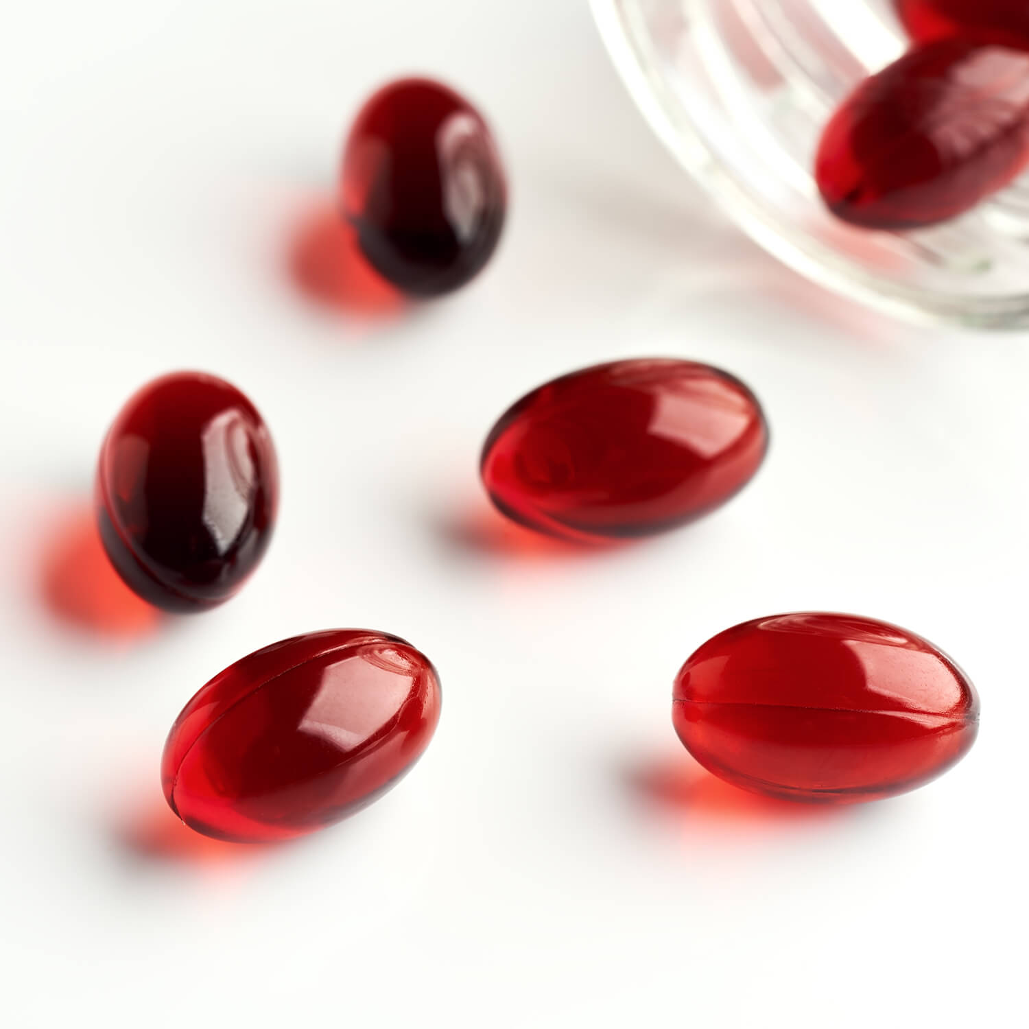 Red gel capsules scattered on a white surface.