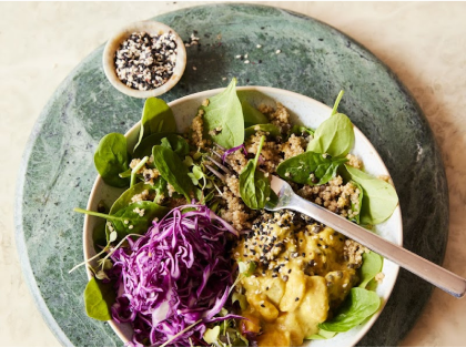 A quinoa salad with spinach, purple cabbage, and creamy dressing on a green marble surface.