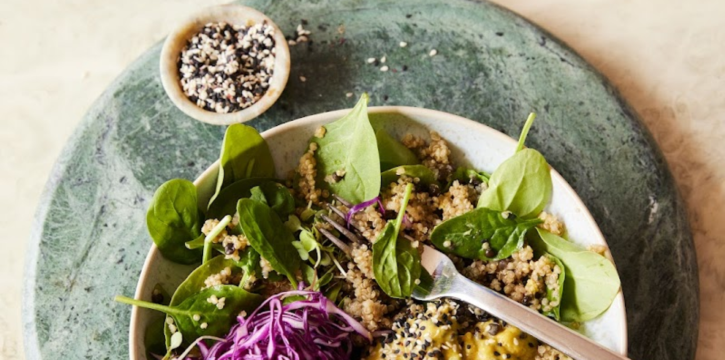 A bowl of quinoa salad with spinach, cabbage, and sesame seeds.