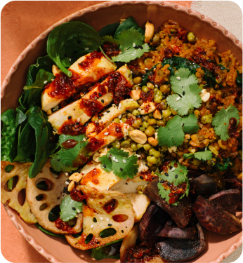 A colorful vegetarian dish with grilled halloumi, quinoa, spinach, lotus root, and cilantro garnish.