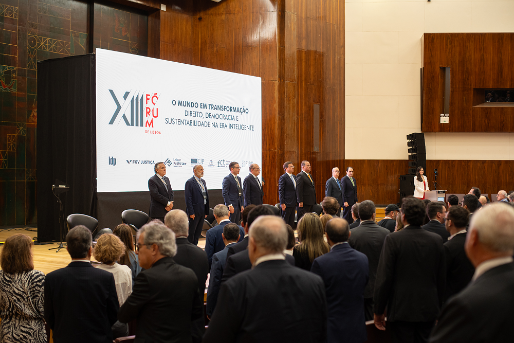 A group of men stand on a stage in front of a large screen and an audience.