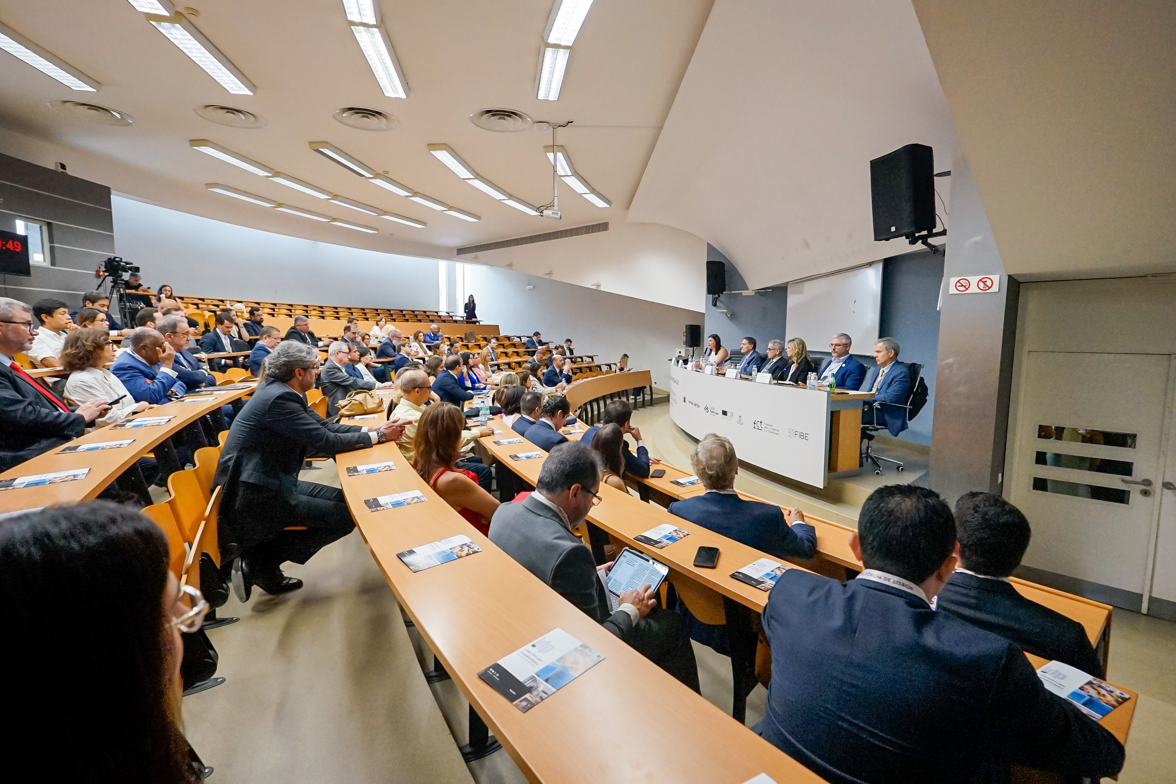 A wide shot of a conference in a tiered lecture hall with a panel and a large audience.