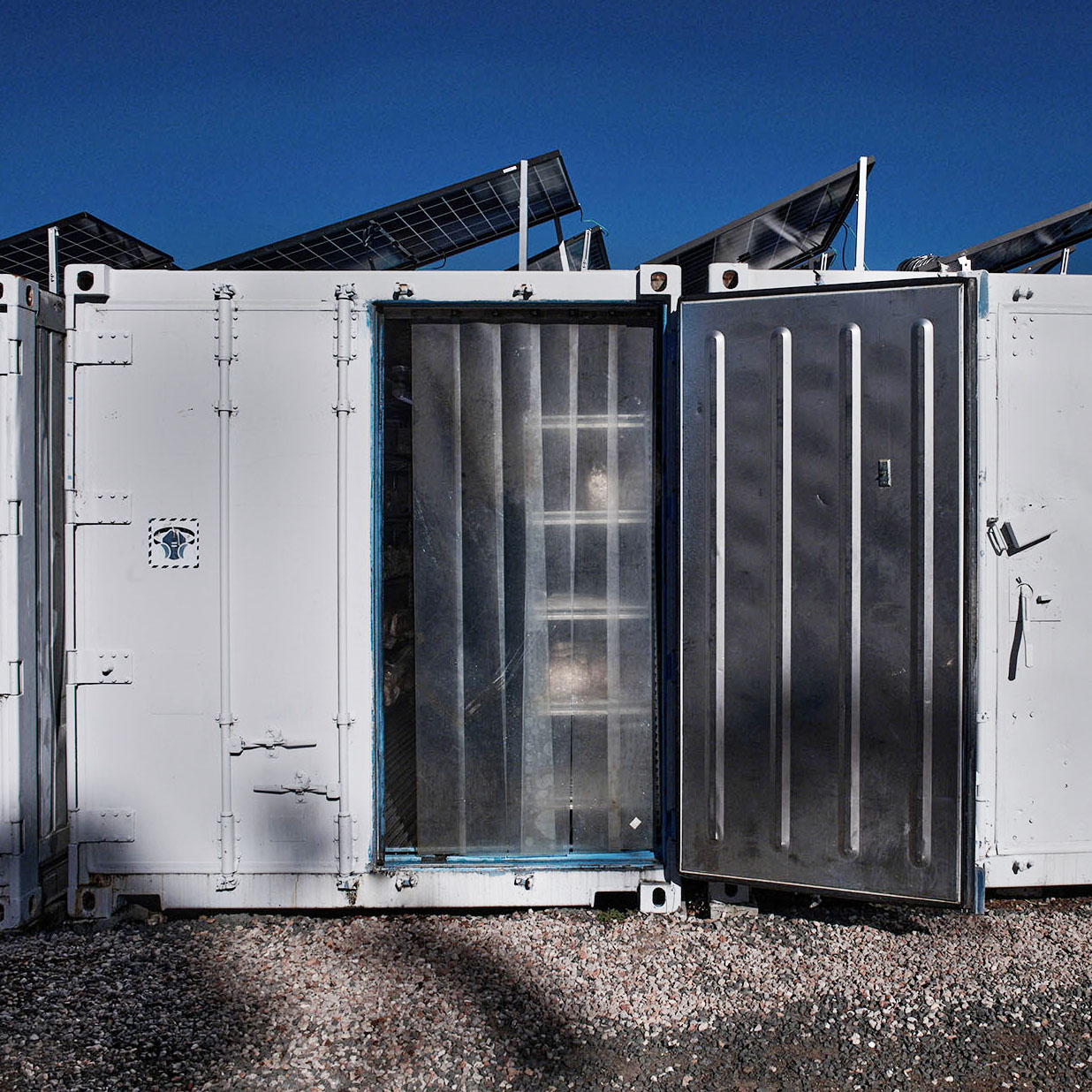 White shipping container with open door, solar panels on top.