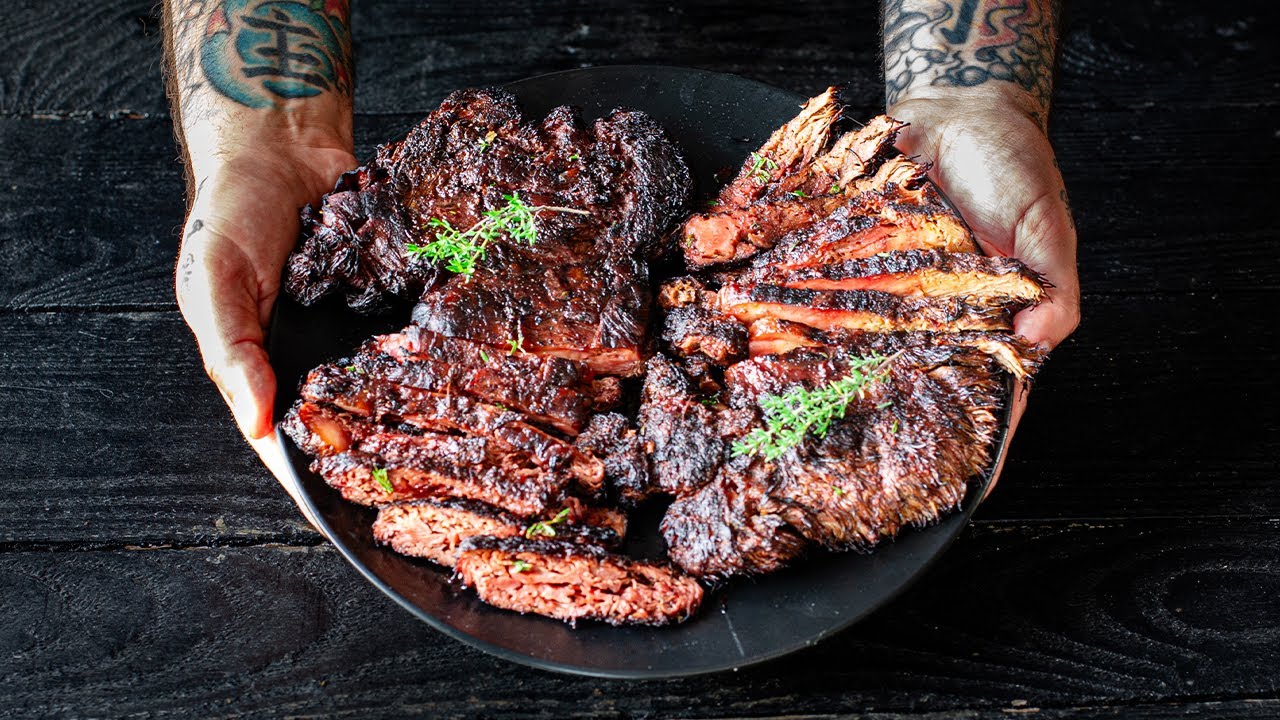 Two tattooed hands holding a plate of grilled sliced meat.