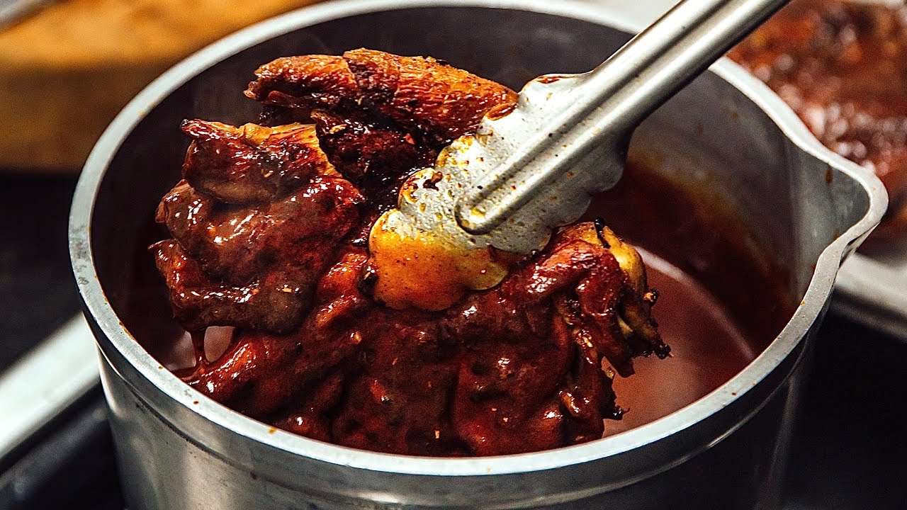 Tongs holding cooked chicken in a metal pot with sauce.