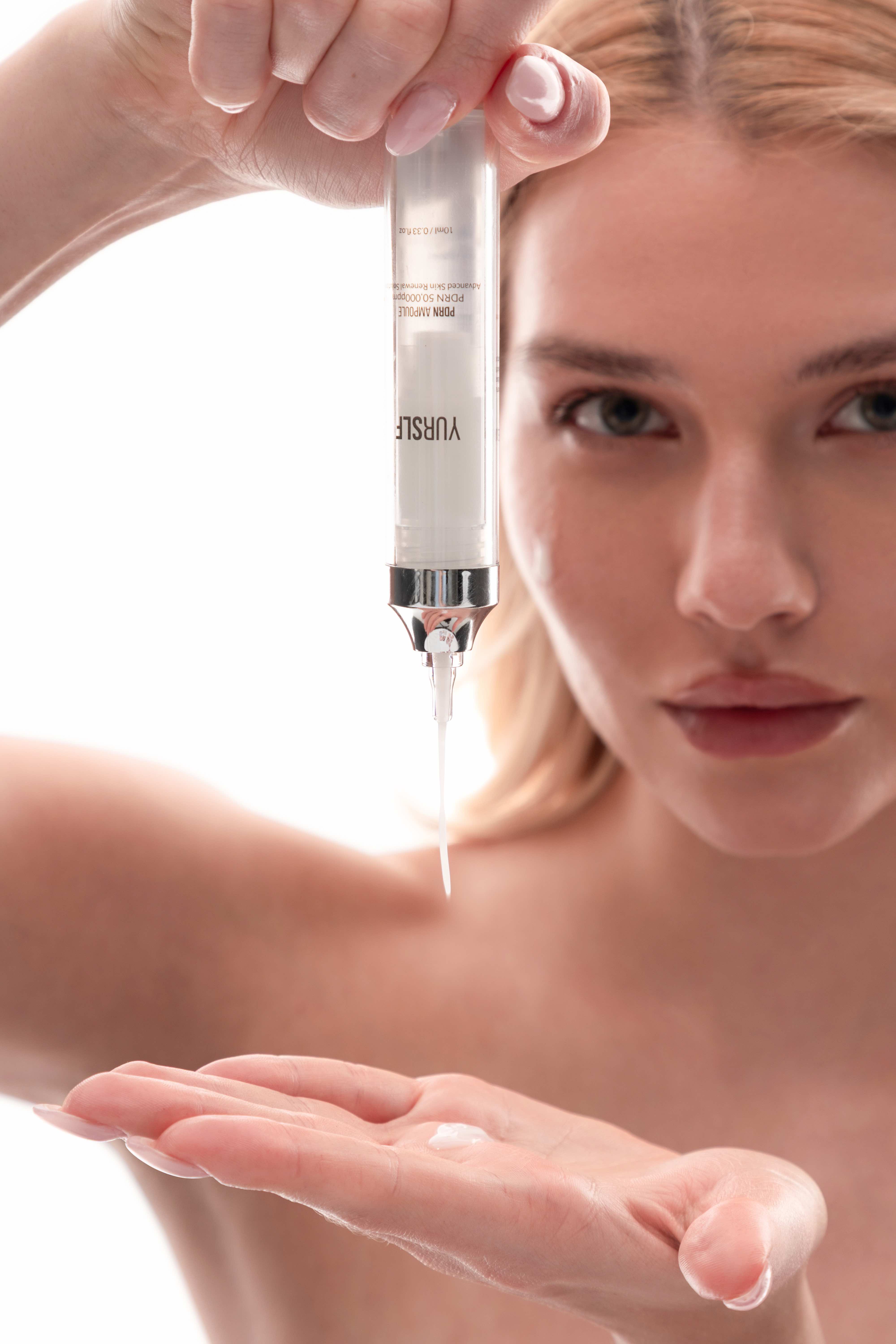 A woman dispenses a skincare product from a syringe-like container into her hand.