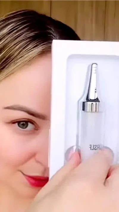 A woman peeks from behind a white box containing a cosmetic applicator bottle.