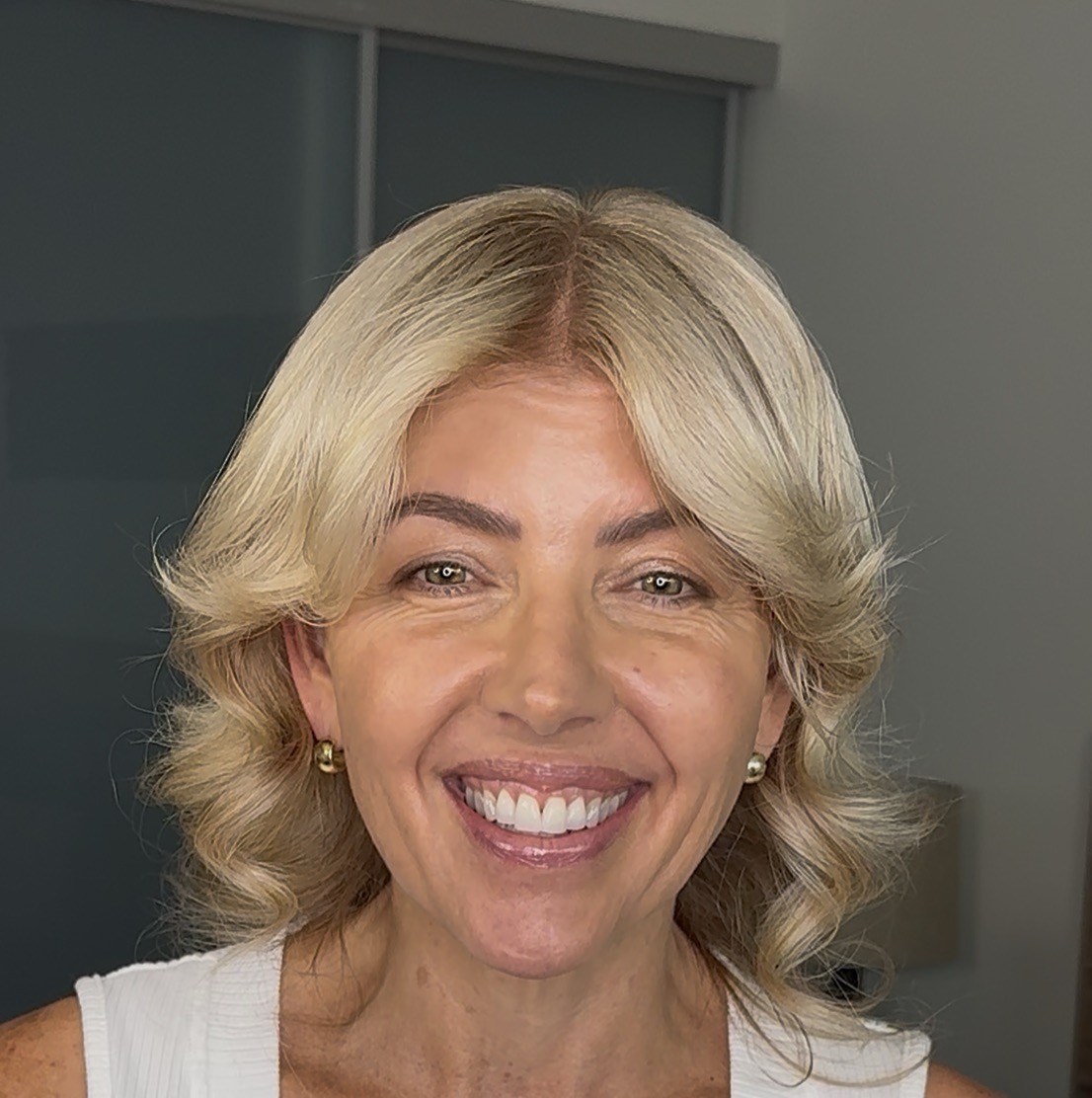 A smiling woman with styled blonde hair and green eyes looks at the camera.