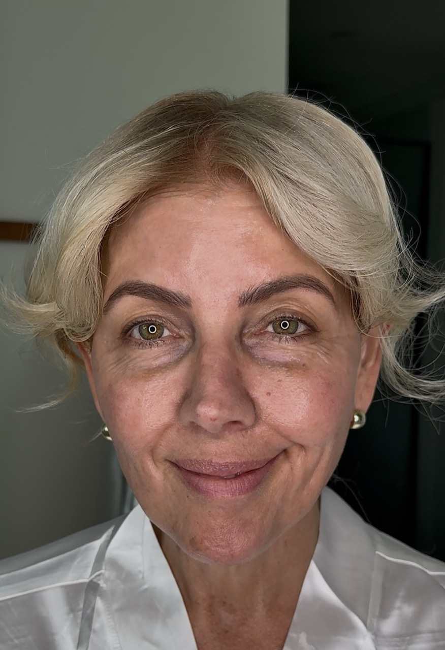 A close-up headshot of a smiling woman with short blonde hair and green eyes wearing a white shirt.