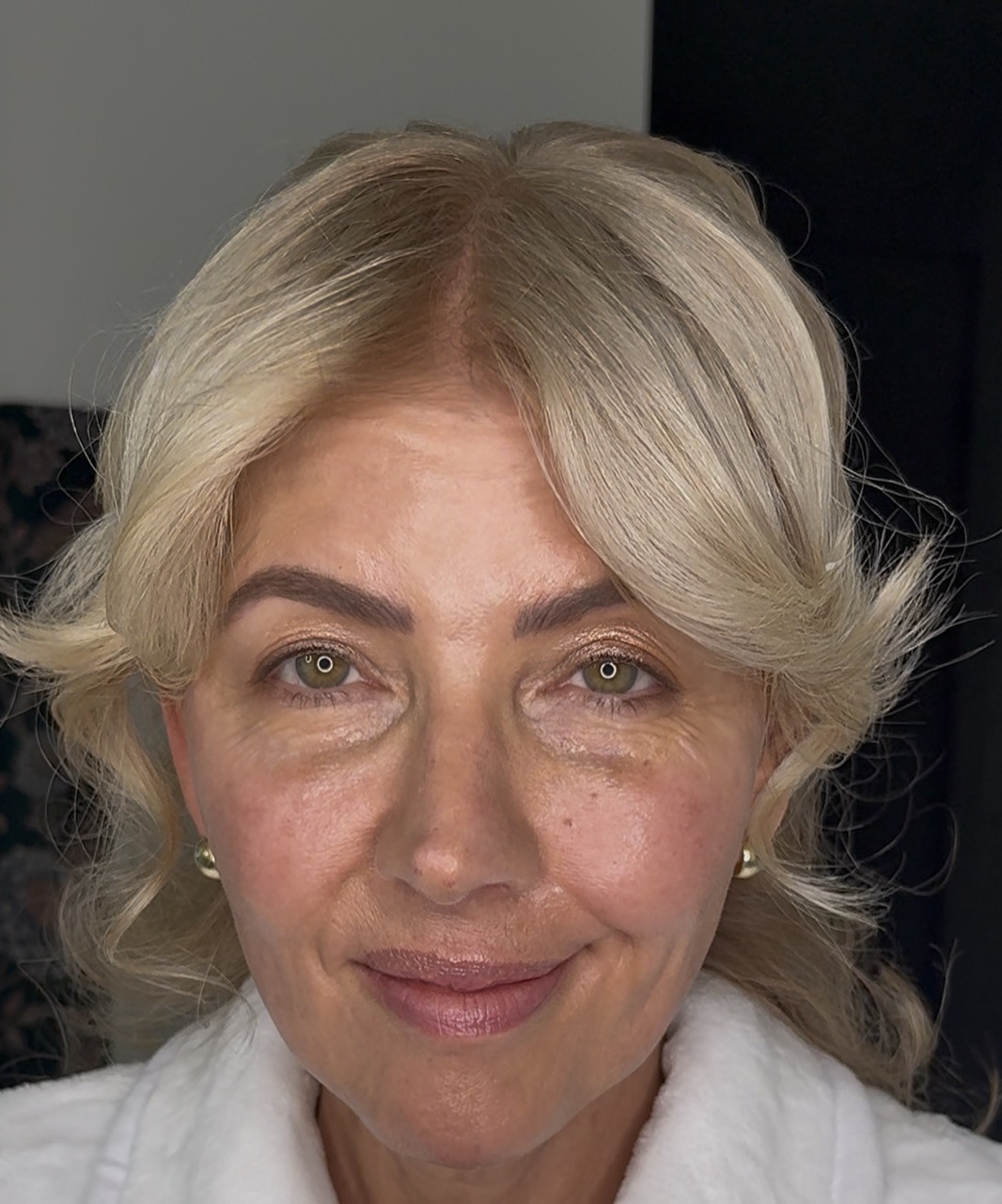 A close-up portrait of a smiling woman with blonde hair, green eyes, and wearing a white robe.