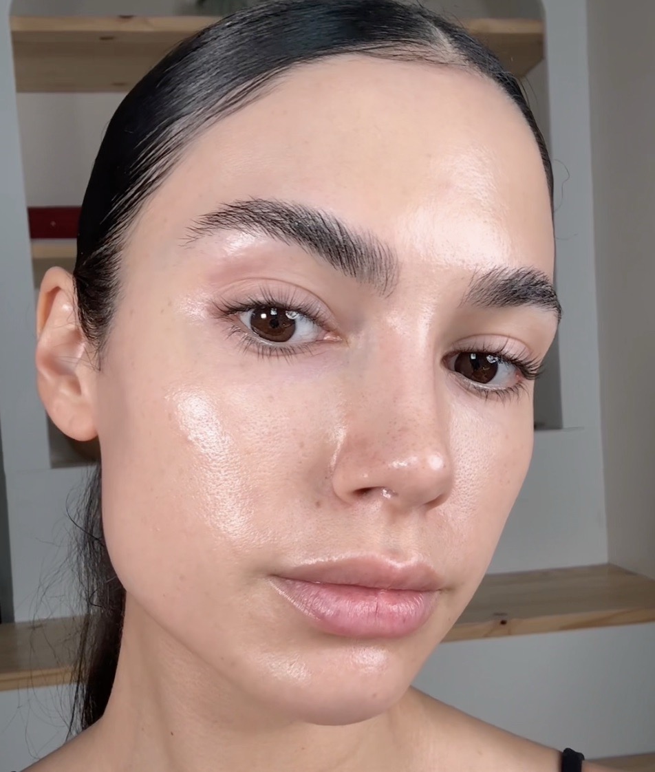 A close-up photo of a woman with very dewy, glowing skin and dark hair pulled back.