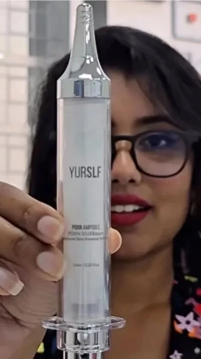 A woman holds up a large, syringe-shaped cosmetic container labeled YURSLF.