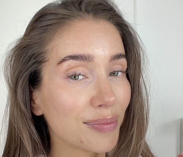 A close-up of a woman with brown hair, green eyes, and glossy lips, looking at the camera.