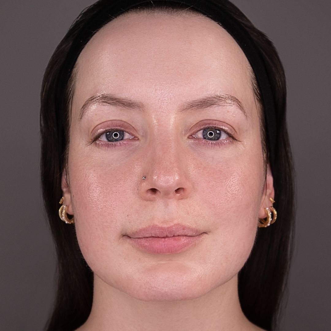 A close-up of a woman's face. She has blue eyes, a nose stud, and gold hoop earrings.