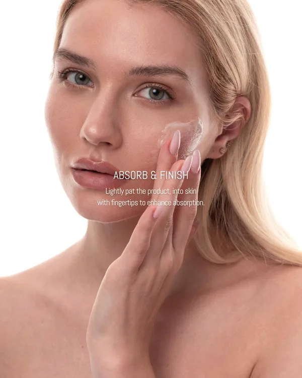 A close-up of a woman with blonde hair applying a clear product to her cheek with her fingertips.
