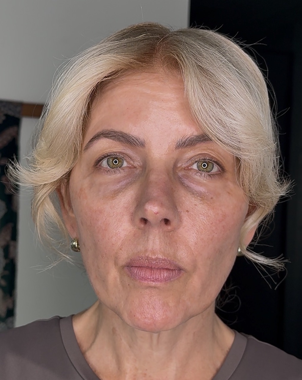 A close-up portrait of a woman with short blonde hair and green eyes looking directly at the camera.
