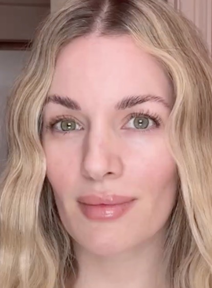 A close-up of a woman with wavy blonde hair and green eyes looking forward.