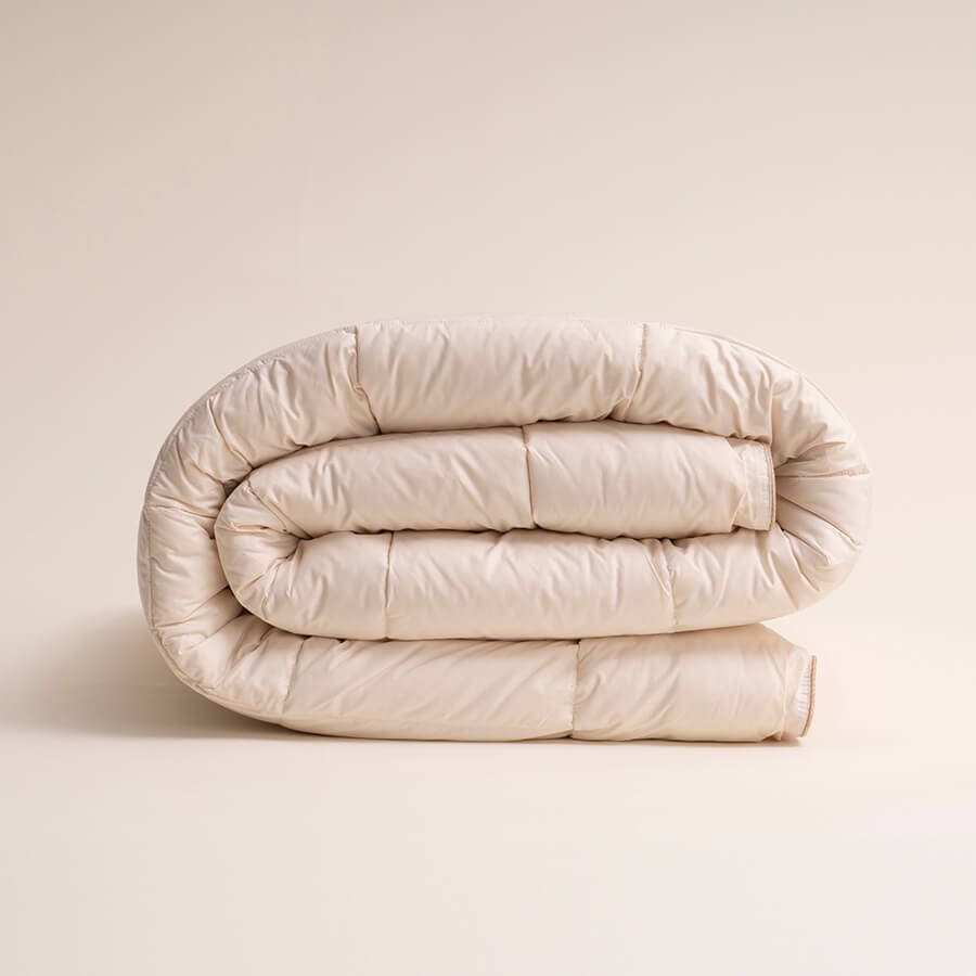 A neatly rolled, beige comforter on a plain background.