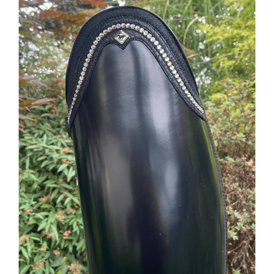 Close-up of a shiny black boot with decorative trim, outdoors.