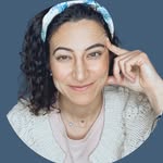 Person with curly hair and a headband, resting their head on their hand, smiling gently.