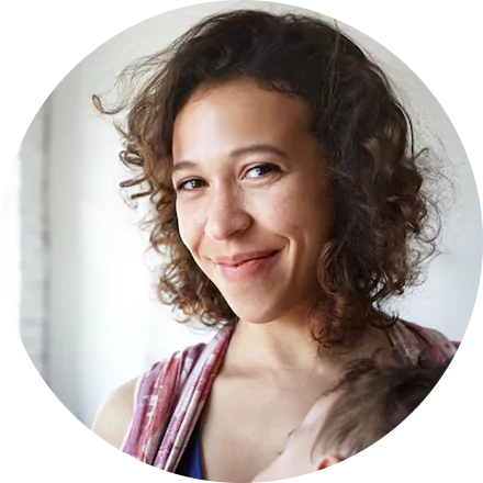 Smiling person with curly hair holding a child, indoors.