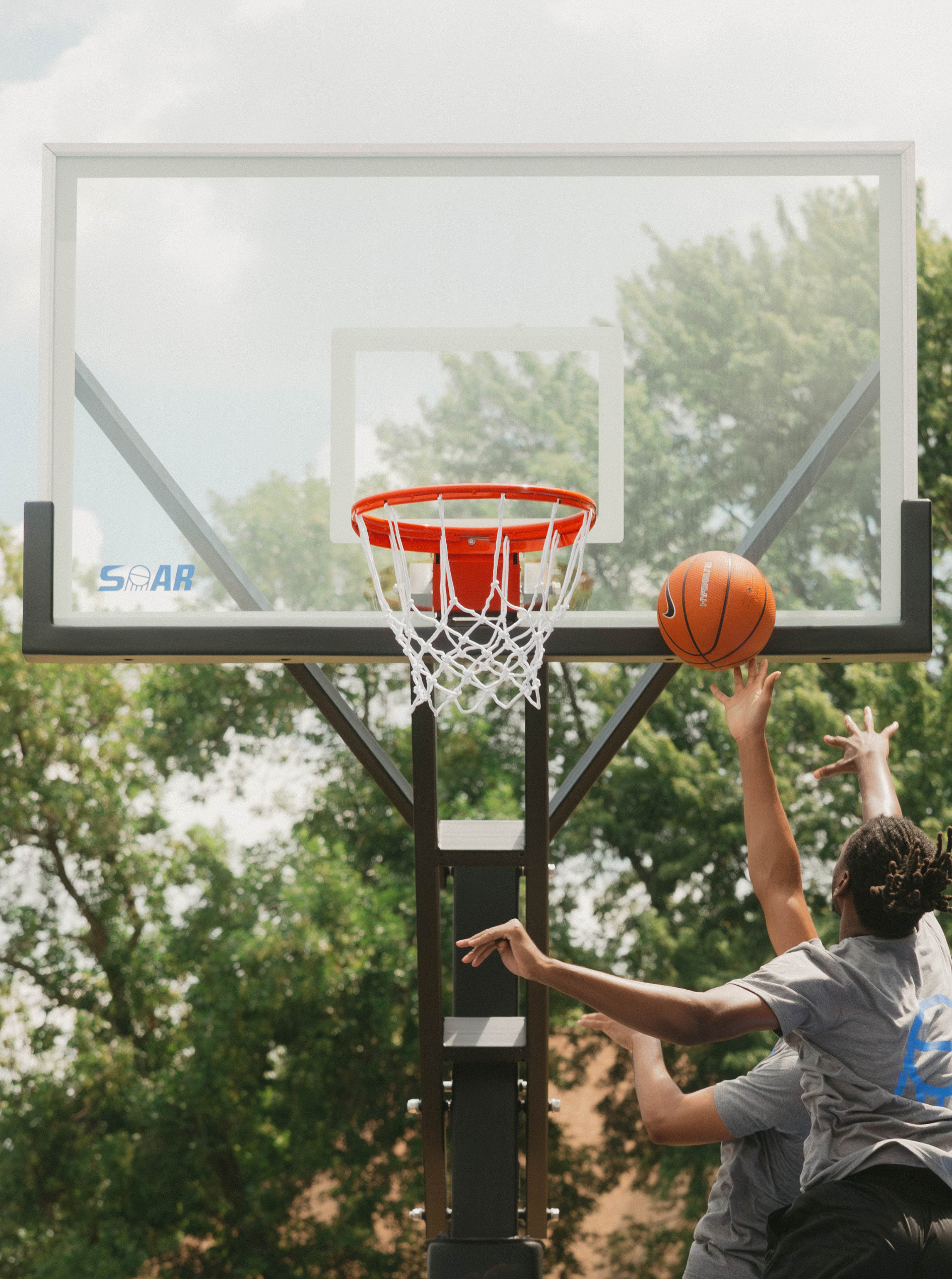 Two people playing basketball outdoors, one shooting near the hoop.