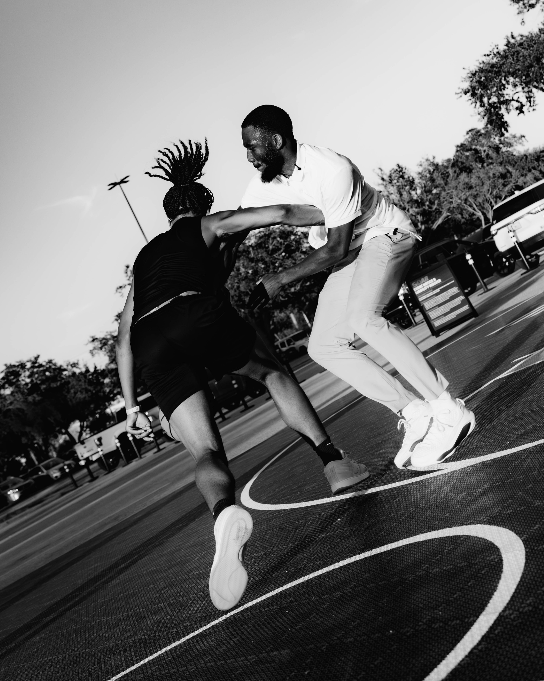 Two people playing basketball outdoors in black and white.