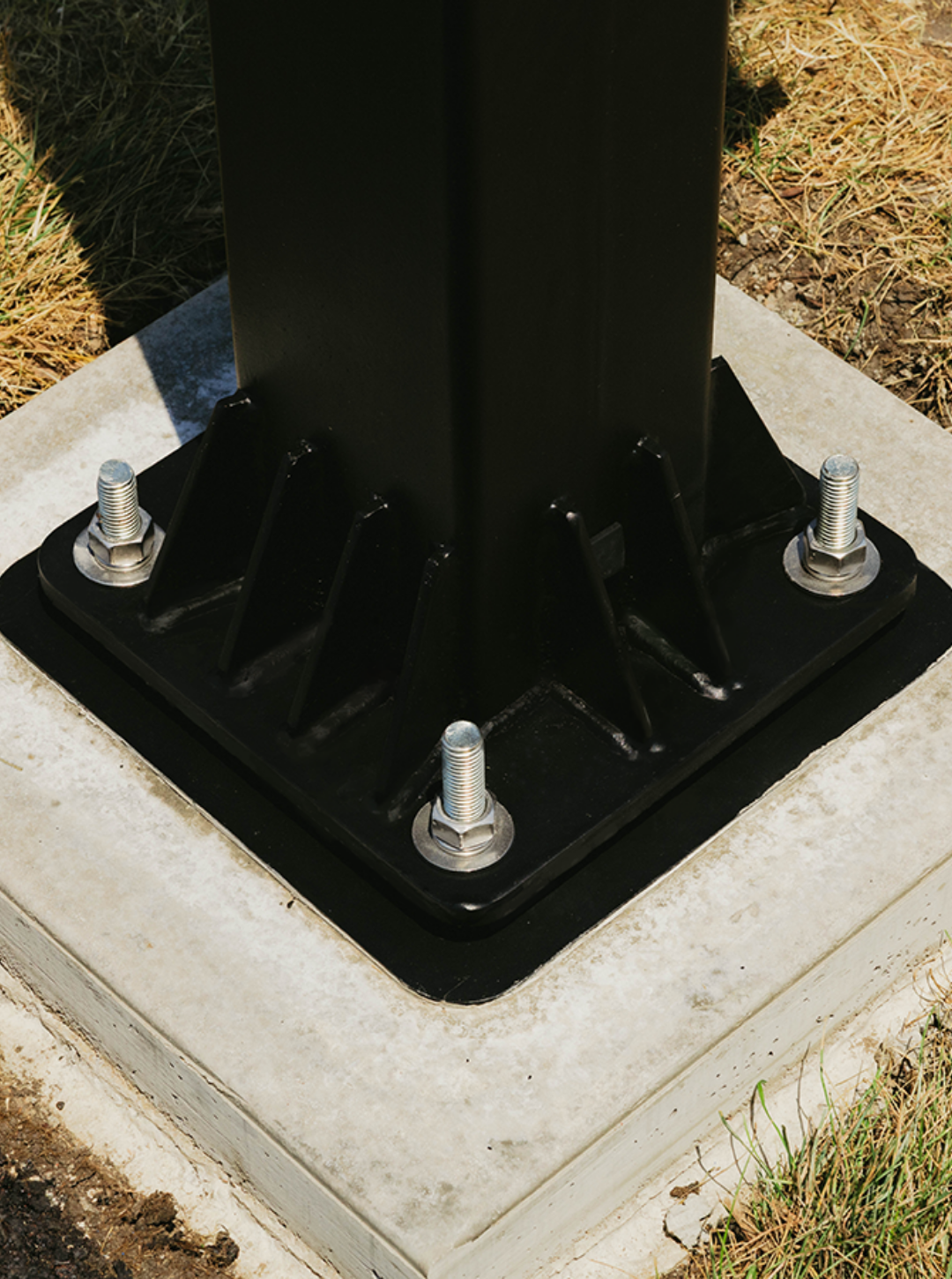 Black metal post base bolted to concrete foundation.
