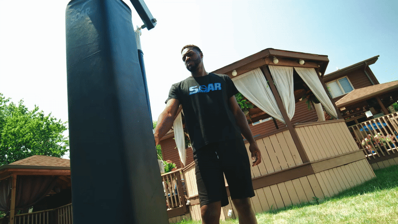 Man in black shirt standing near a punching bag outdoors.