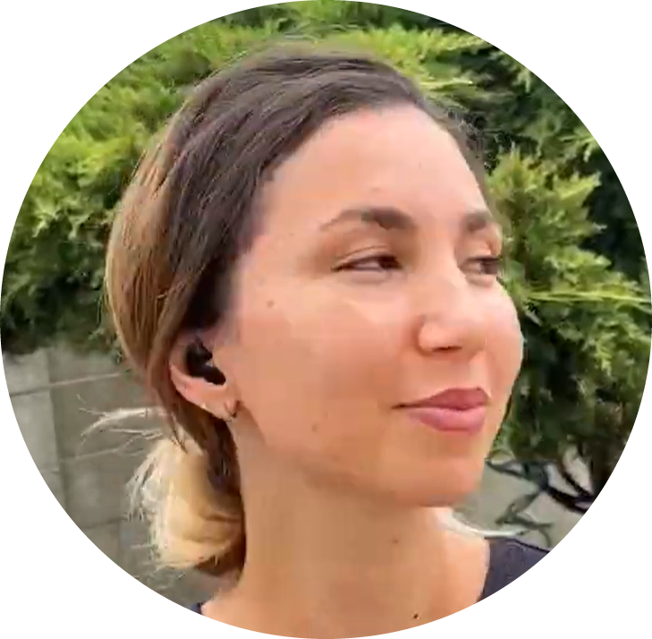 Person outdoors wearing earbuds, greenery in the background.