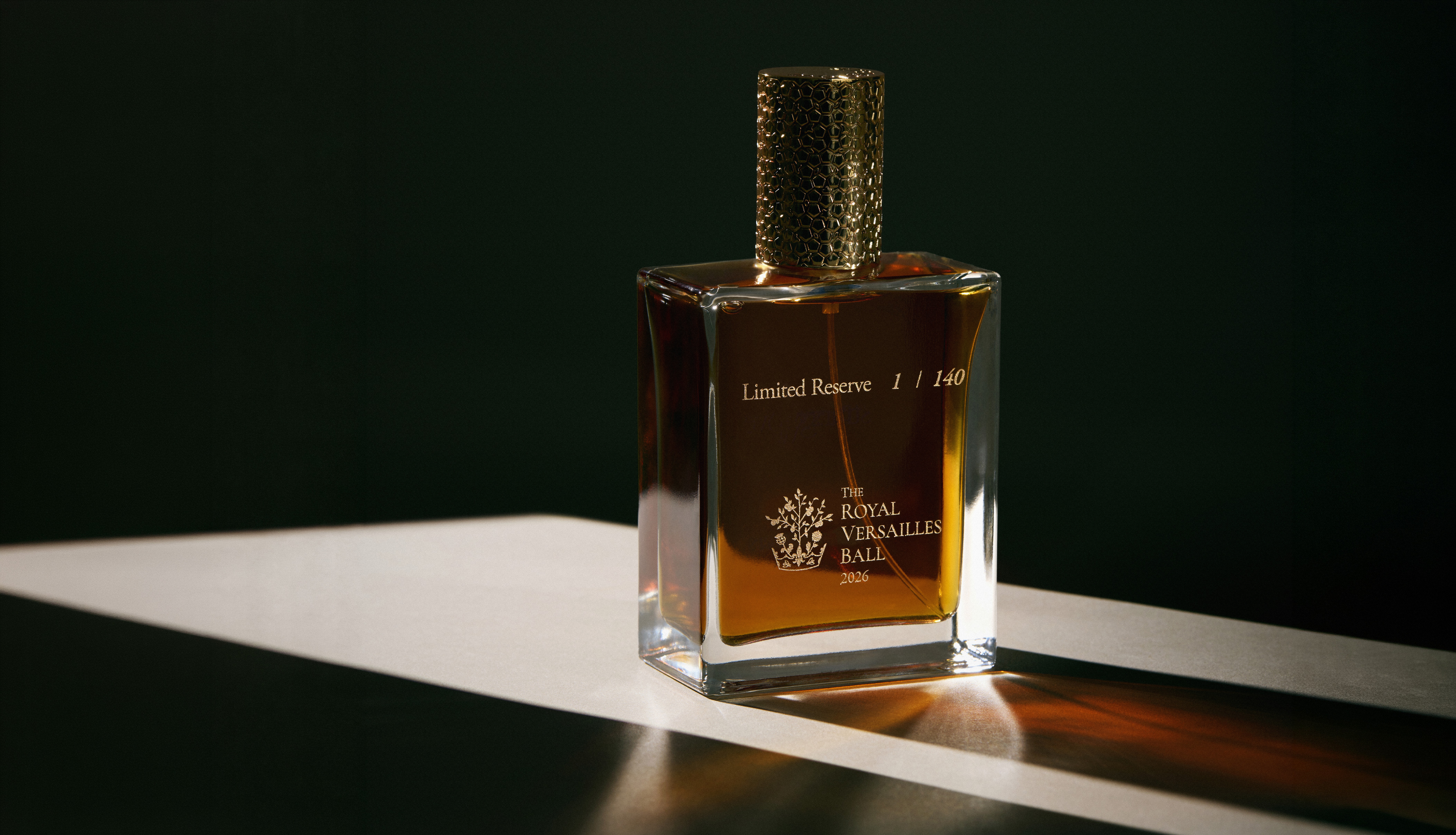 A square glass perfume bottle with a textured gold cap, sitting in a diagonal band of light.