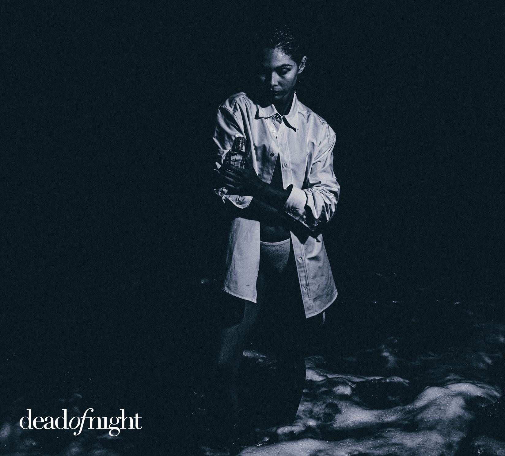 Person in a white shirt holding an object, standing in water at night.