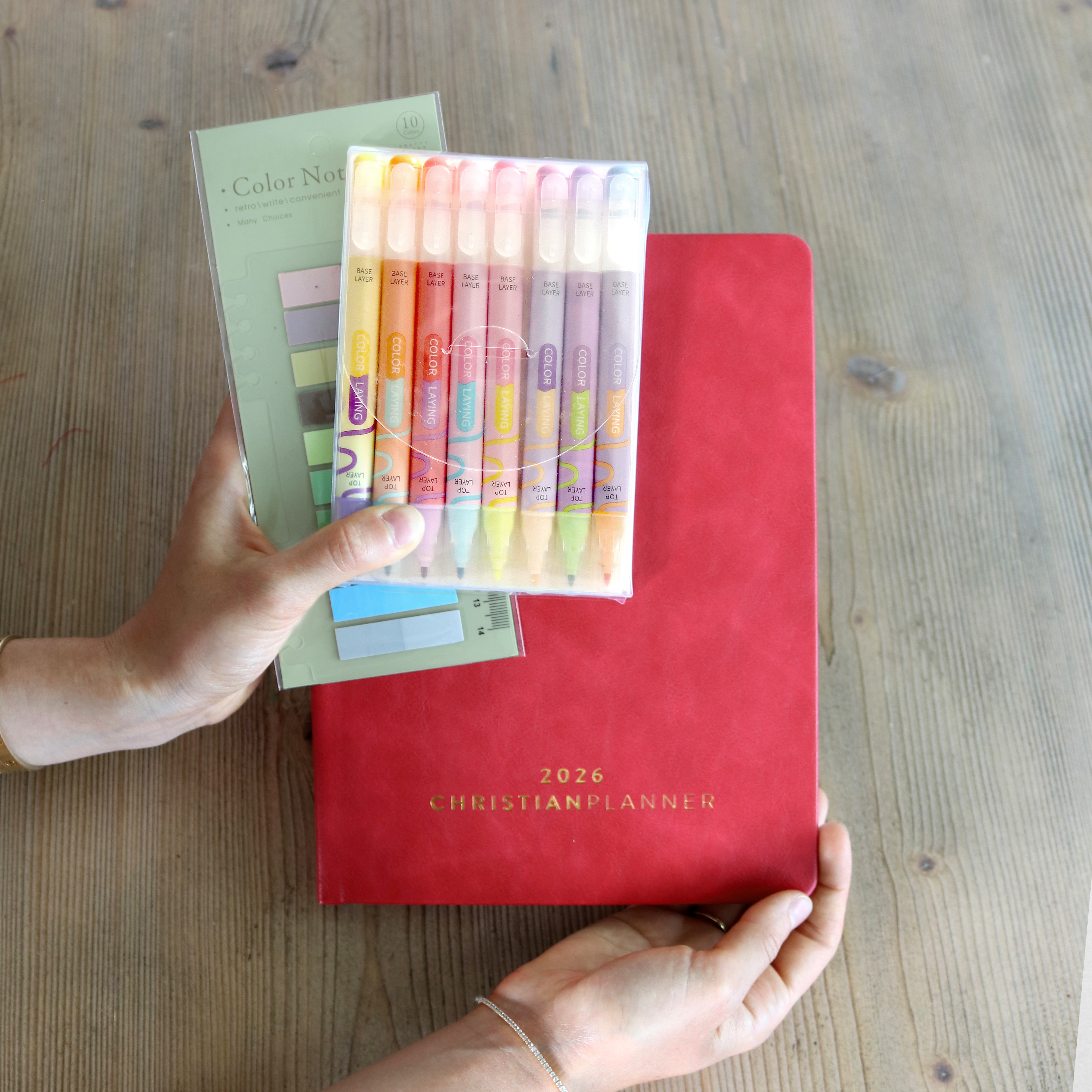 Hands holding a 2026 planner, colored pens, and sticky notes.