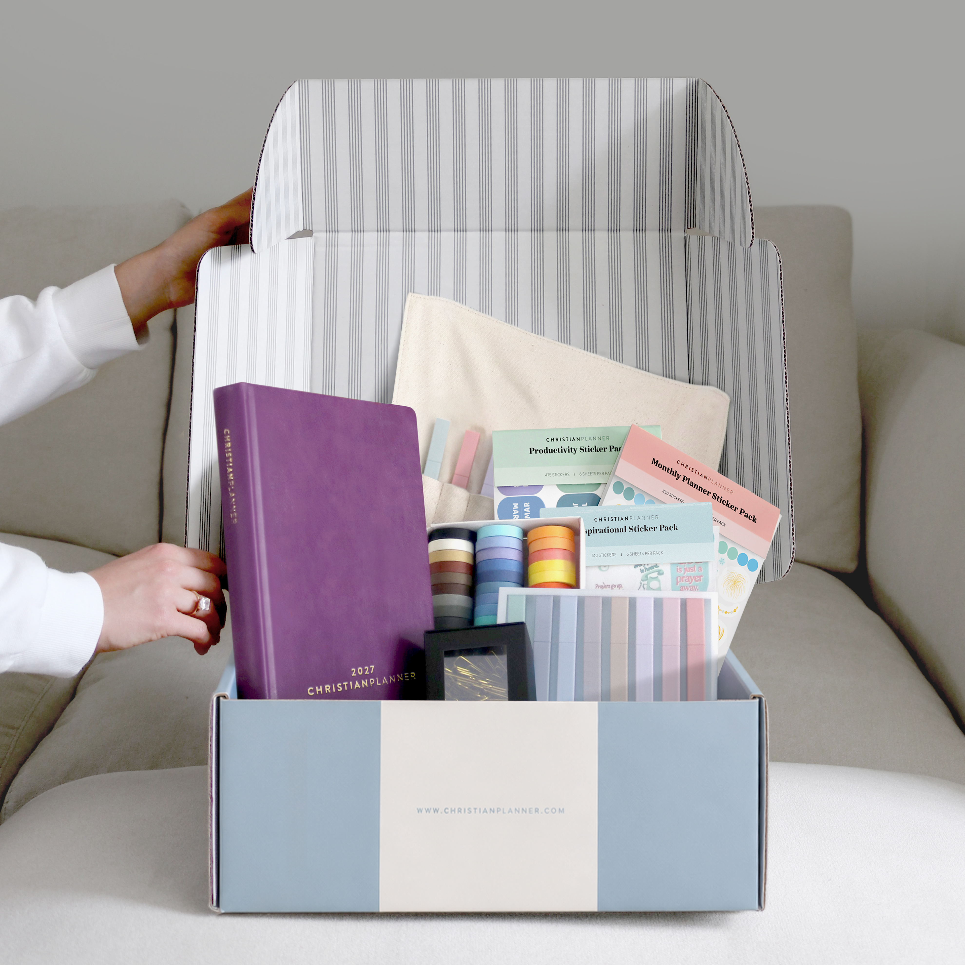 A person unboxing a Christian Planner gift set containing a planner, stickers, washi tape, and other stationery.