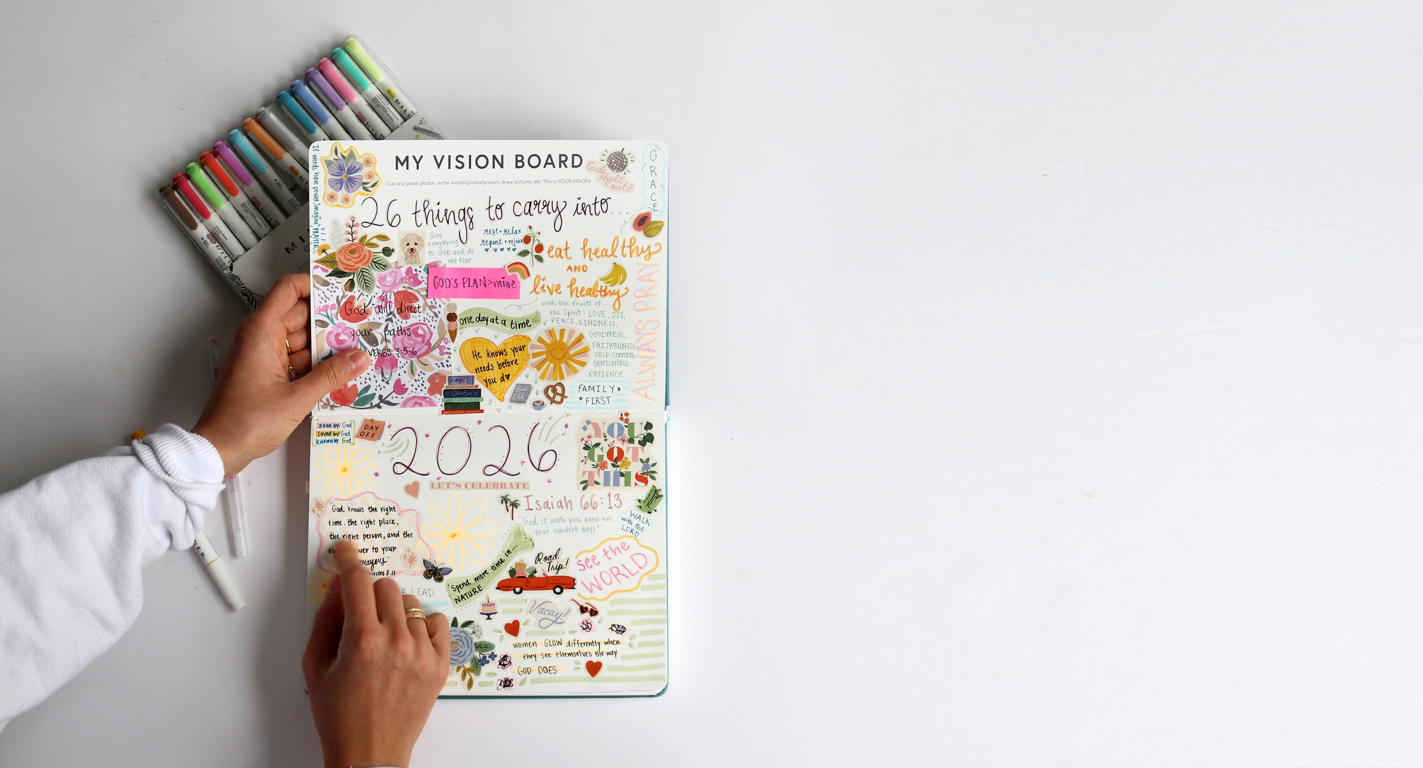 An overhead view of a person creating a colorful vision board in an open journal with markers nearby.