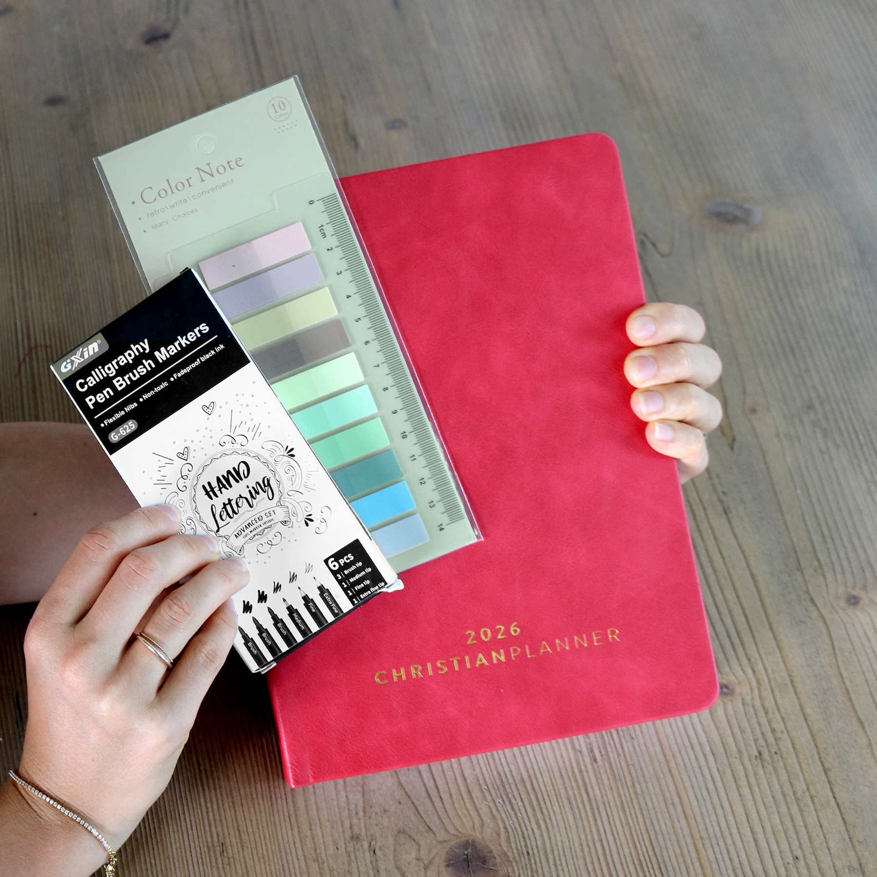 Hands holding a 2026 planner, calligraphy markers, and color note tabs.