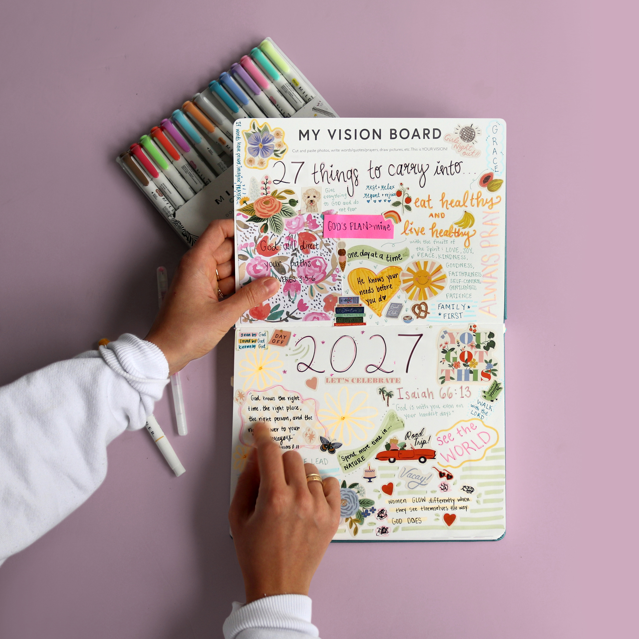 Overhead view of a person creating a colorful vision board in a journal with pens nearby.