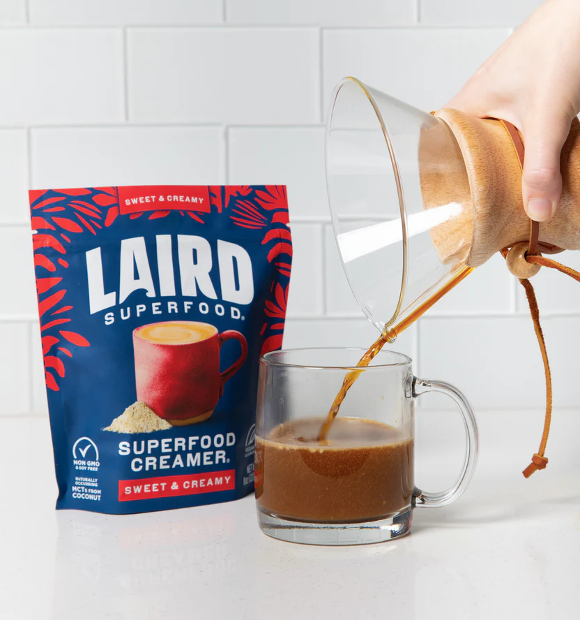 A hand pours coffee into a clear mug next to a bag of Laird Superfood creamer.