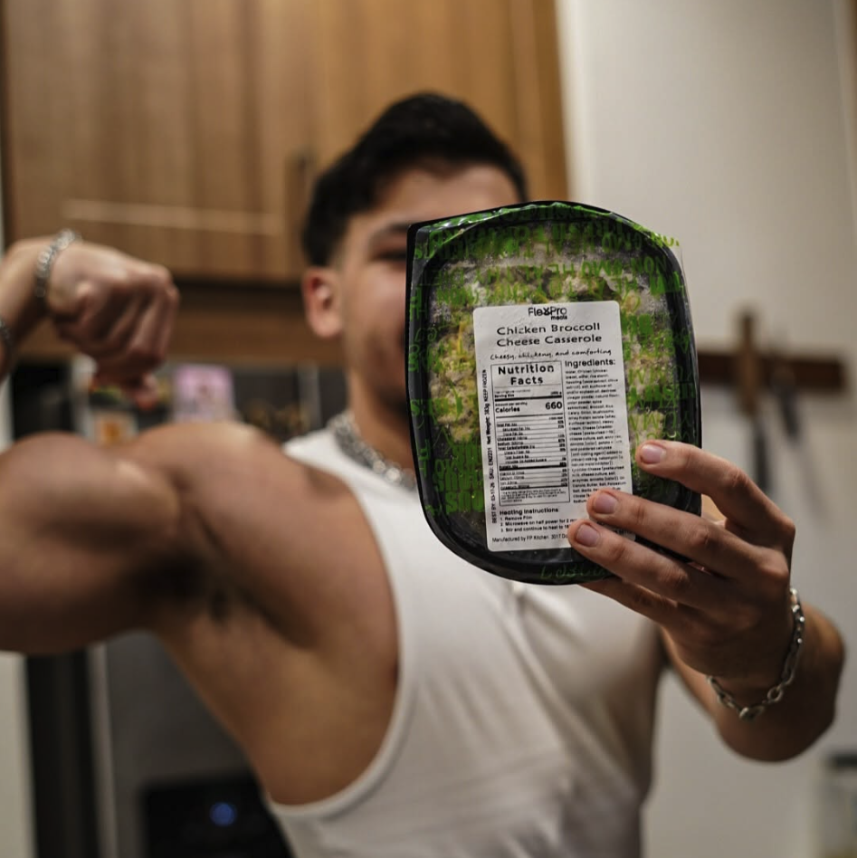 Person flexing arm while holding a packaged meal in front of face.