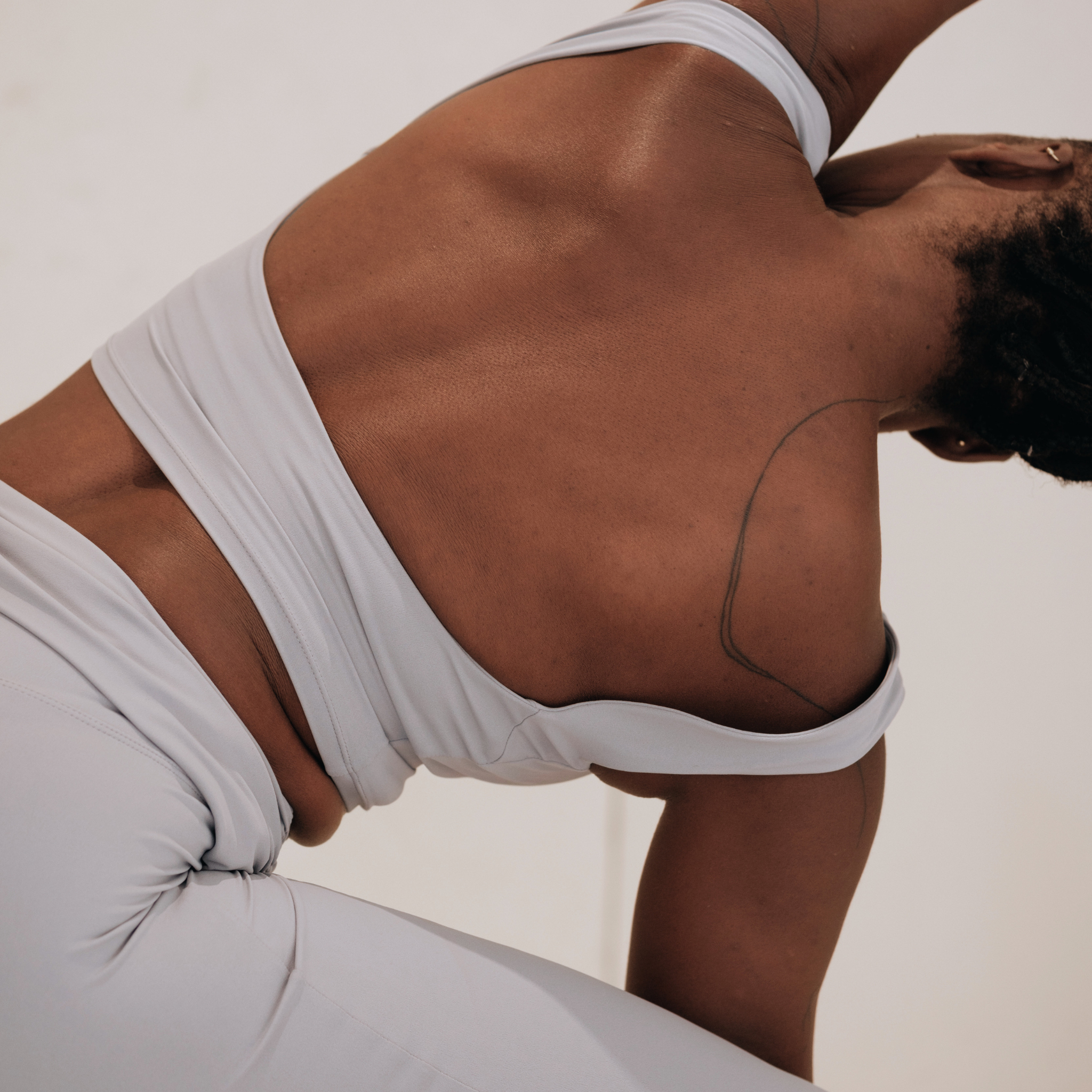 A close-up of a person's back as they twist in light-colored athletic wear against a white background.