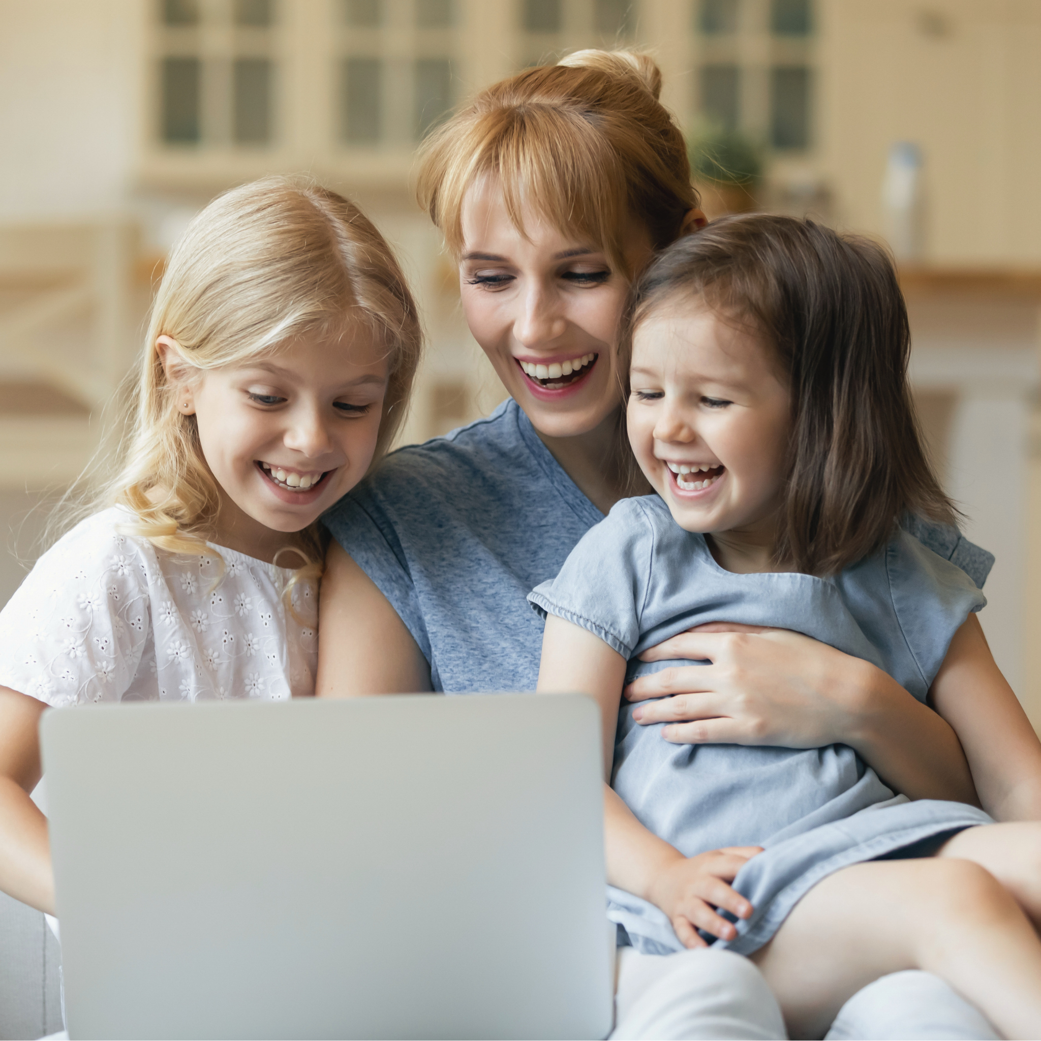 A woman and two young girls are laughing while looking at a laptop.