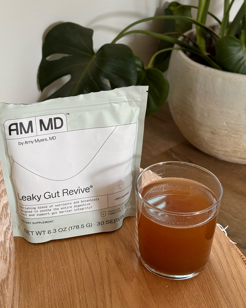 A pouch of Leaky Gut Revive dietary supplement next to a glass of the drink on a table.