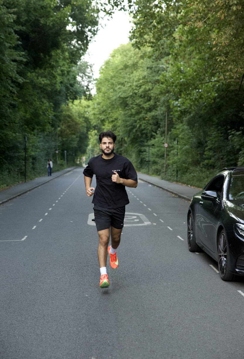 Man jogging on a tree-lined road beside a parked car.