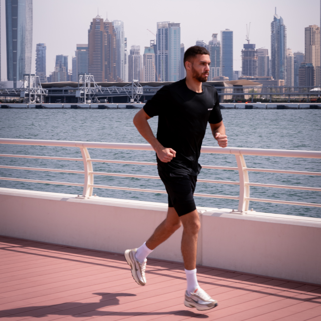Man jogging on a waterfront path with city skyline in the background.