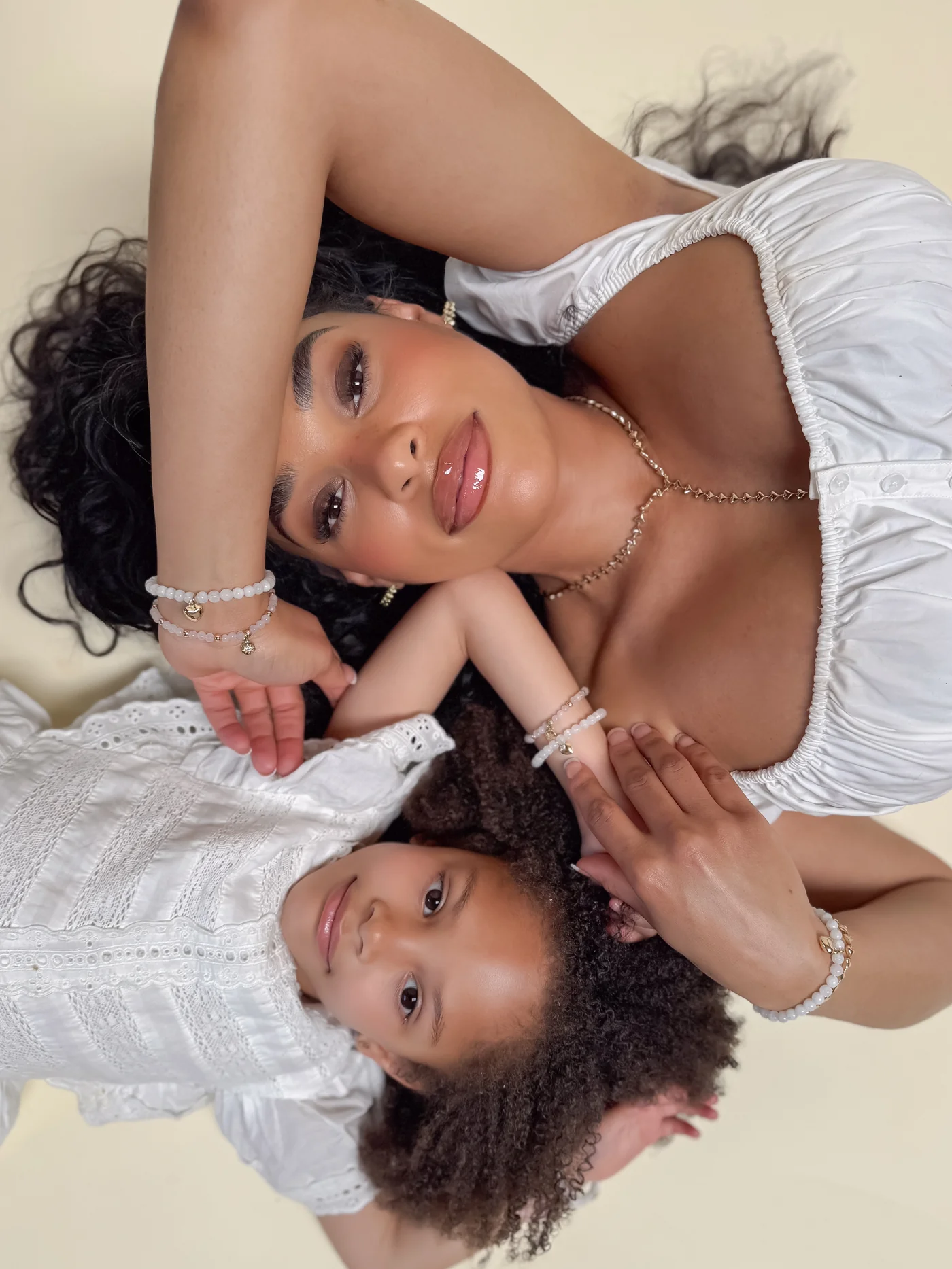 Woman and child lying down, wearing white clothes and bracelets, looking at the camera.