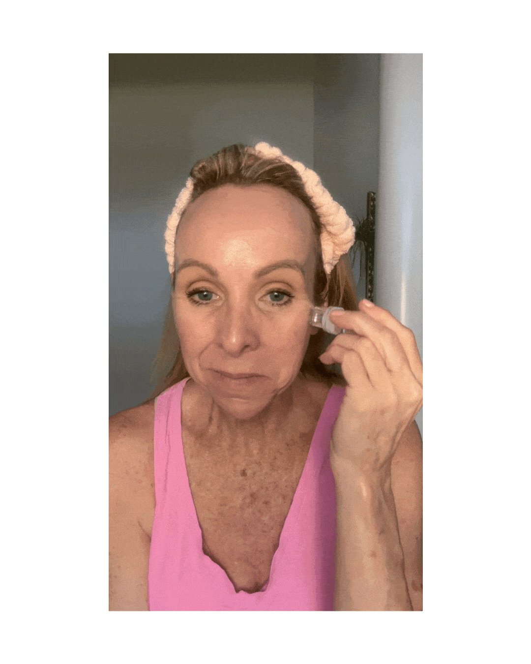 Person uses a beauty tool on their cheek while wearing a pink headband and top.