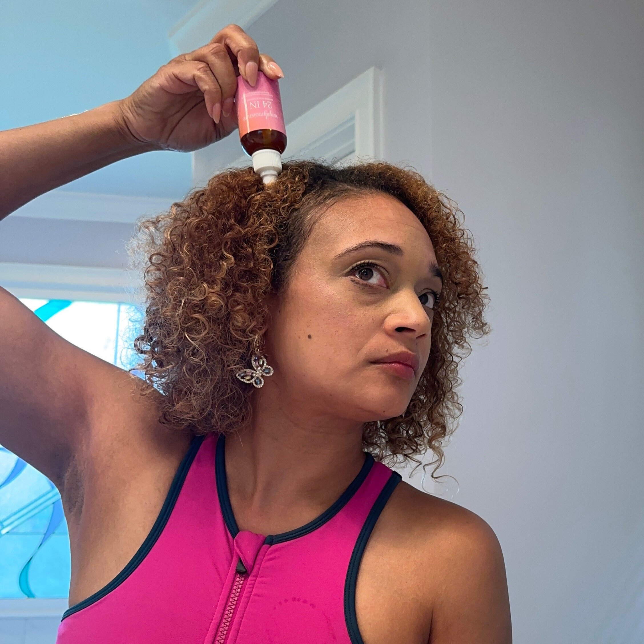 Person applying hair product to curly hair in a bathroom.
