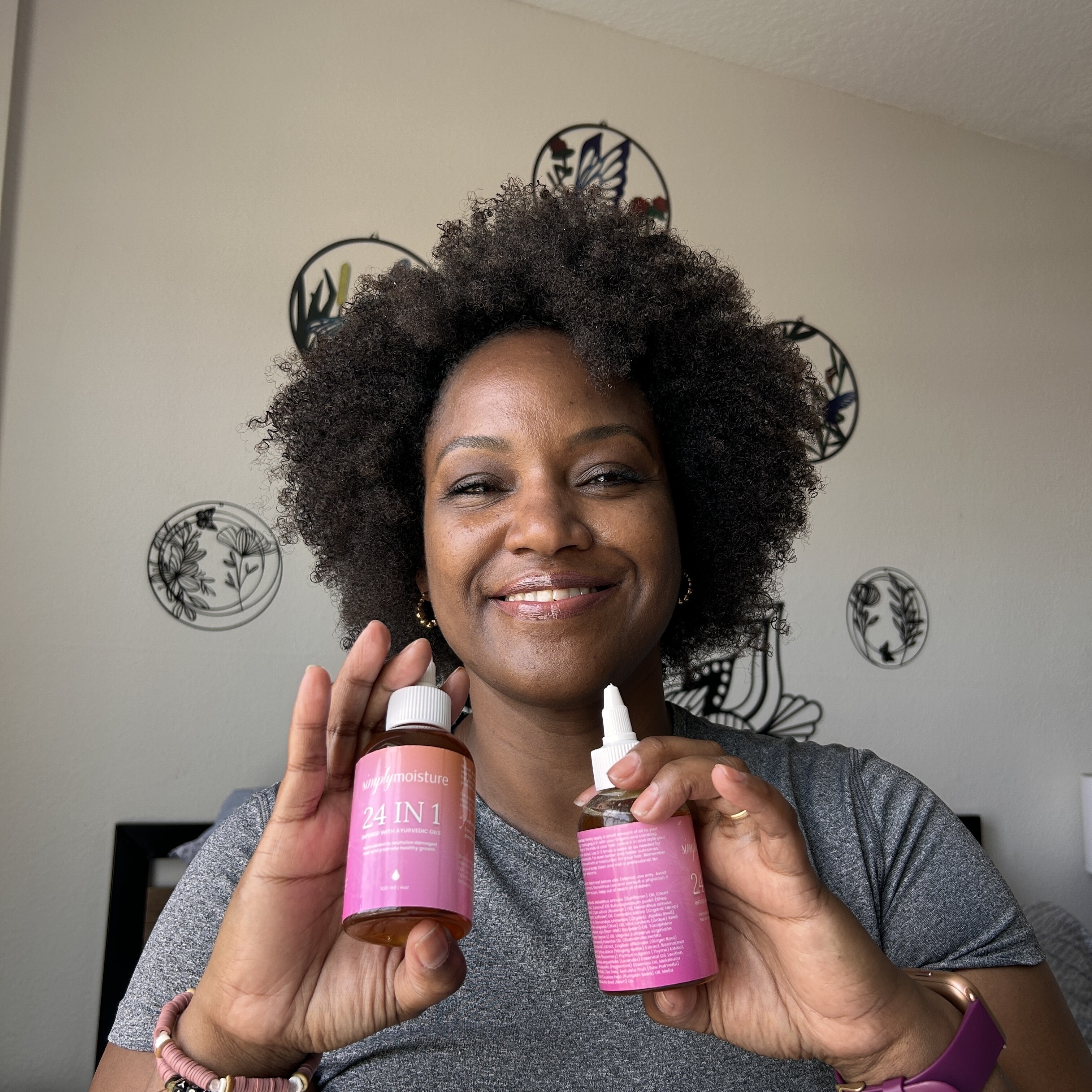 Person smiling and holding two pink-labeled bottles indoors.