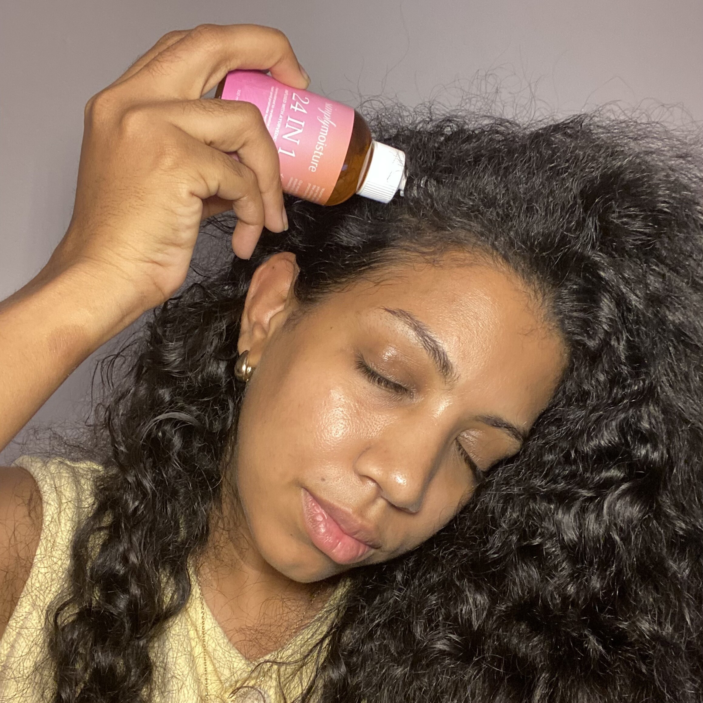 Person applying hair oil to scalp with eyes closed.