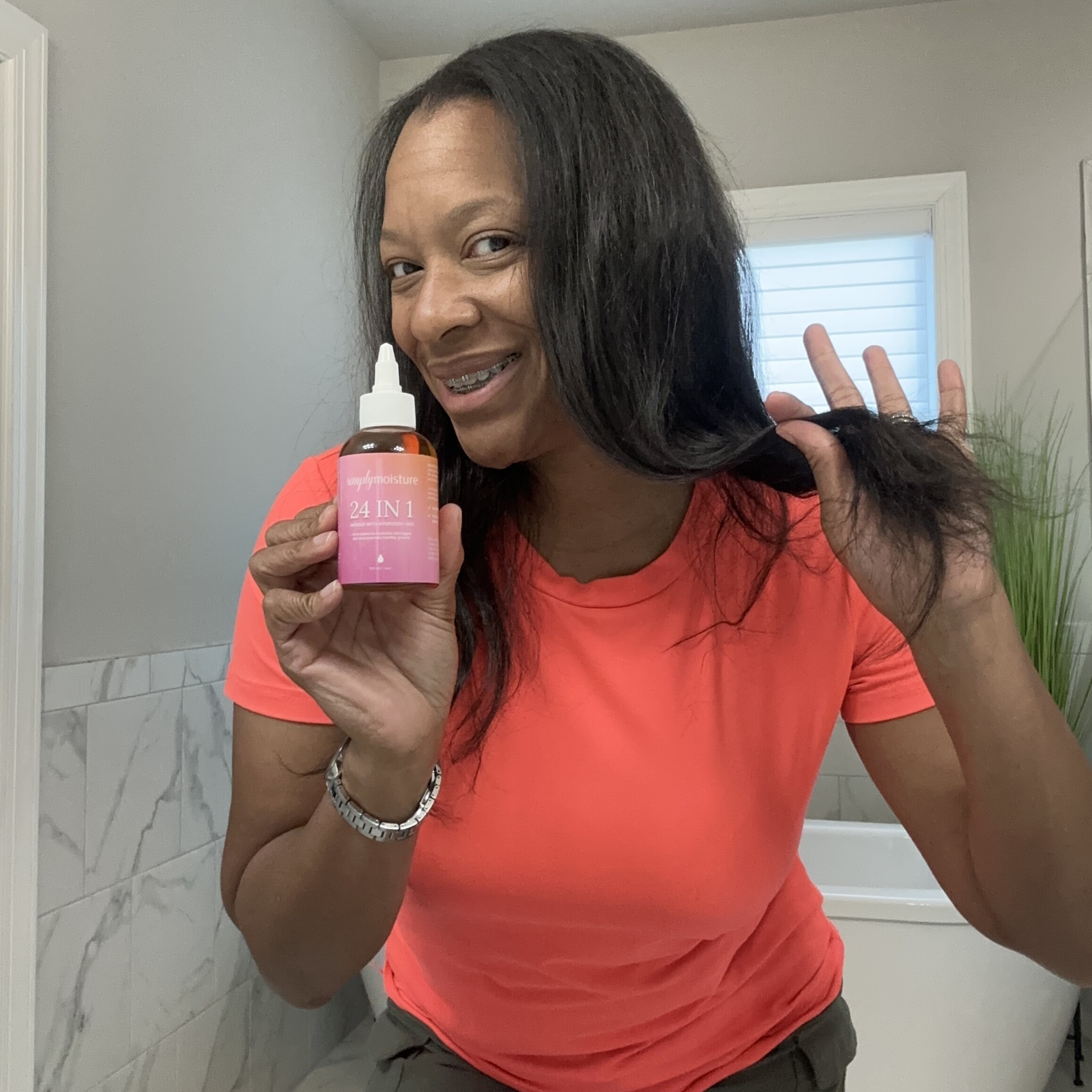 Person holding a hair product bottle, smiling in a bathroom.